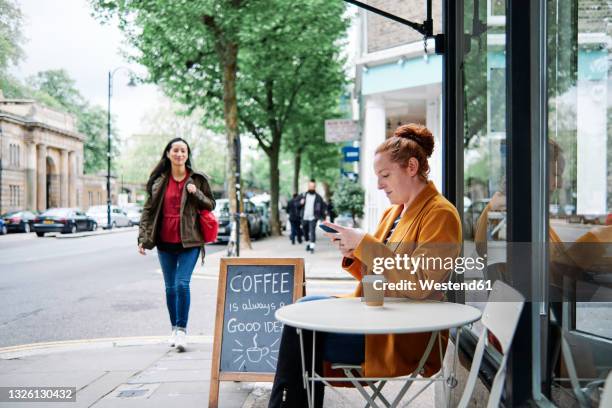 woman using mobile phone at sidewalk cafe - pavement cafe stock pictures, royalty-free photos & images