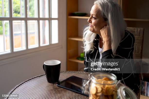 senior woman contemplating while sitting at table in living room - westend 61 fotografías e imágenes de stock