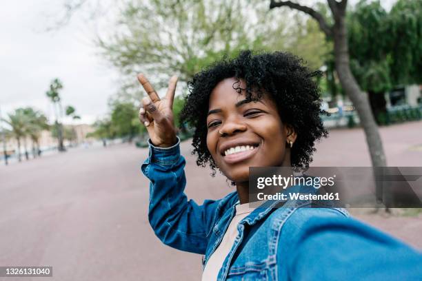 happy woman showing peace sign while taking selfie - selfie frau stock-fotos und bilder