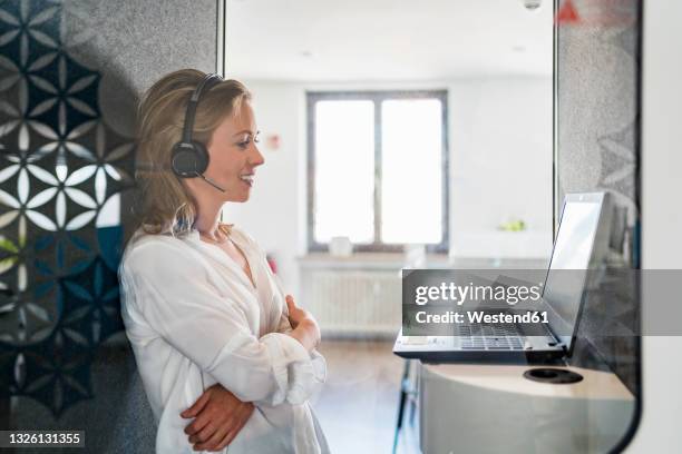 smiling female customer service representative with arms crossed standing in front of laptop at office - soundproof stock pictures, royalty-free photos & images