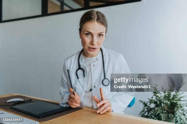 female doctor discussing while sitting at desk - female doctor portrait stock pictures, royalty-free photos & images