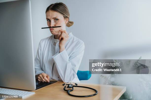 female doctor playing with pen while sitting at desk - doctor humor stock pictures, royalty-free photos & images