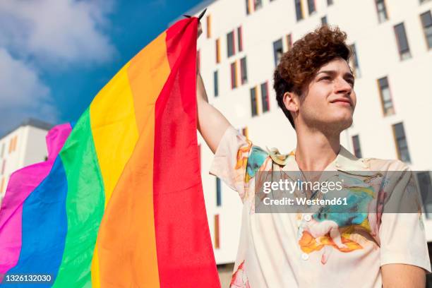 young man looking away while blowing rainbow flag - cérémonie du drapeau photos et images de collection