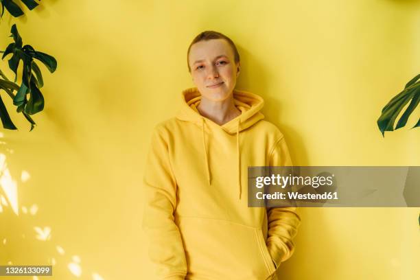 young woman with hands in pockets against yellow wall - hooded shirt ストックフォトと画像