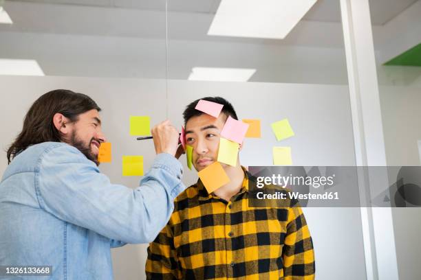 mischievous male professional writing on adhesive notes sticking on male coworker face - sticky stock pictures, royalty-free photos & images