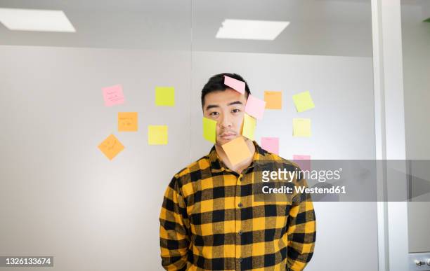 young businessman standing with adhesive notes sticking on face - sticky stock pictures, royalty-free photos & images
