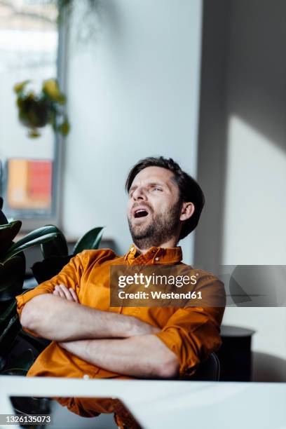 businessman yawing while sitting with arms crossed in office - yawn office stock pictures, royalty-free photos & images