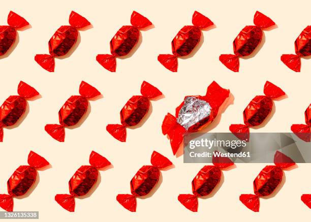 pattern of rows of red wrapped candies with single empty wrapper - chocolate wrapper stock pictures, royalty-free photos & images