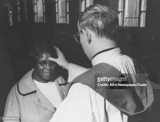 Photograph of a woman kneeling before a Catholic priest who is applying ashes to her forehead as part of the Ash Wednesday service, Ash Wednesday...