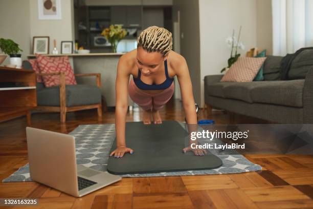 shot of a young woman using a laptop while doing push-up exercises at home - mat stockfoto's en -beelden