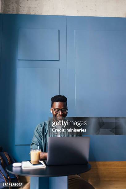 happy businessman with wireless earphones in ears working in a coffee shop on his laptop computer - homem de azul imagens e fotografias de stock