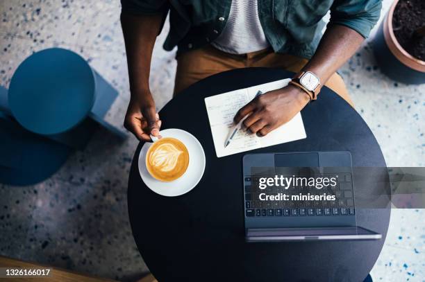 an anonymous businessman holding cappuccino cup while working on his laptop computer in a coffee shop - 21 & over stock pictures, royalty-free photos & images