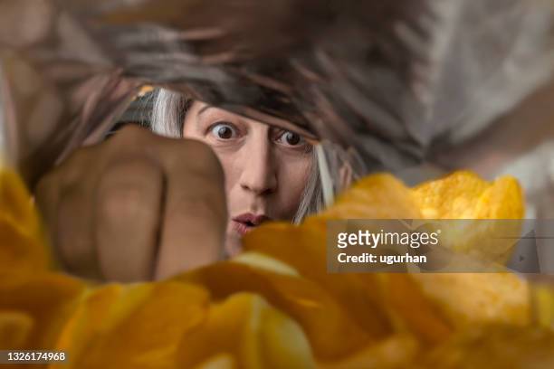 a woman eating chips from a package. - chips bag stockfoto's en -beelden