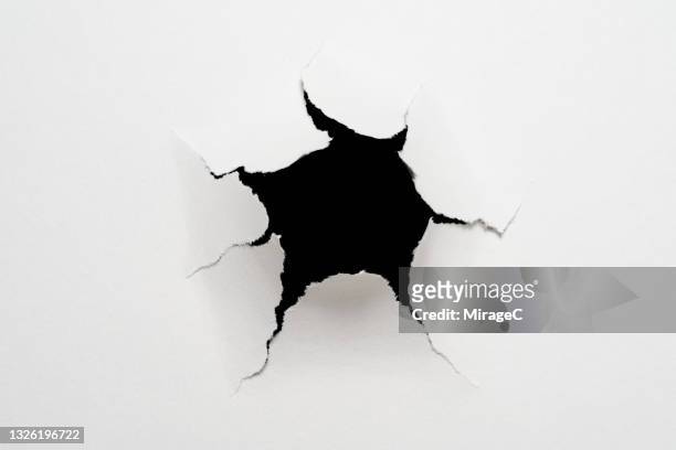 cracked paper hole in front of black - agujero de bala fotografías e imágenes de stock