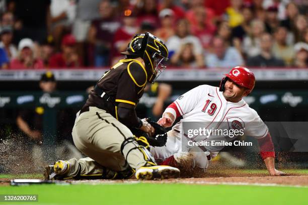 Joey Votto of the Cincinnati Reds slides safely into home base against Victor Caratini of the San Diego Padres for a run in the fourth inning during...