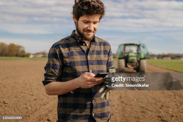 portrait of a farmer using smartphone - tractor in field stockfoto's en -beelden