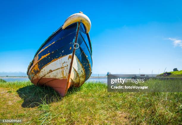 wooden fishing boat on grassy ocean shore lindisfarne island northumberland - northumberland stock pictures, royalty-free photos & images