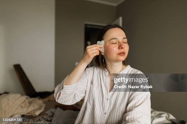 a portrait of a young woman doing gouache massage facial at home - spooning stock pictures, royalty-free photos & images