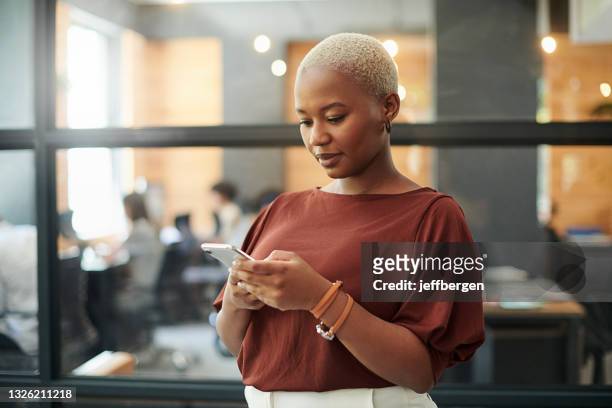 foto de una joven empresaria usando un teléfono inteligente en una oficina moderna - descendencia africana fotografías e imágenes de stock