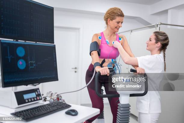 doctora colocando electrodos en el pecho de una mujer - sistema cardiopulmonar humano fotografías e imágenes de stock