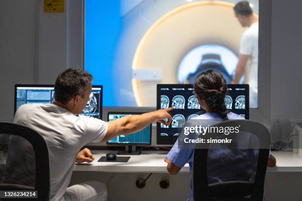 zwei mrt-radiologen sitzen im kontrollraum und bedienen den mrt-scanner - neurowissenschaften stock-fotos und bilder