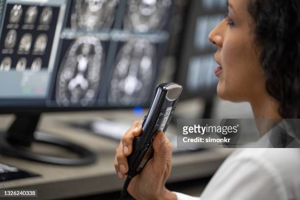 female radiologist speaking into a dictation recorder while looking at mri scan - ditafone imagens e fotografias de stock