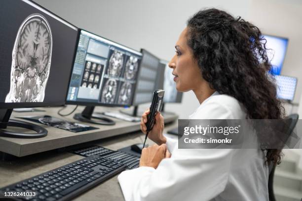 female radiologist speaking into a dictation recorder while looking at mri scan - diktera bildbanksfoton och bilder
