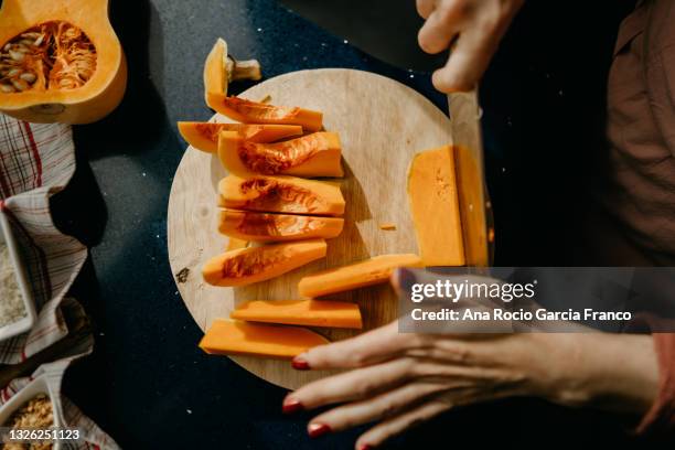 caucasian woman slicing a butternut squash on a wooden cutting board. - taglio foto e immagini stock