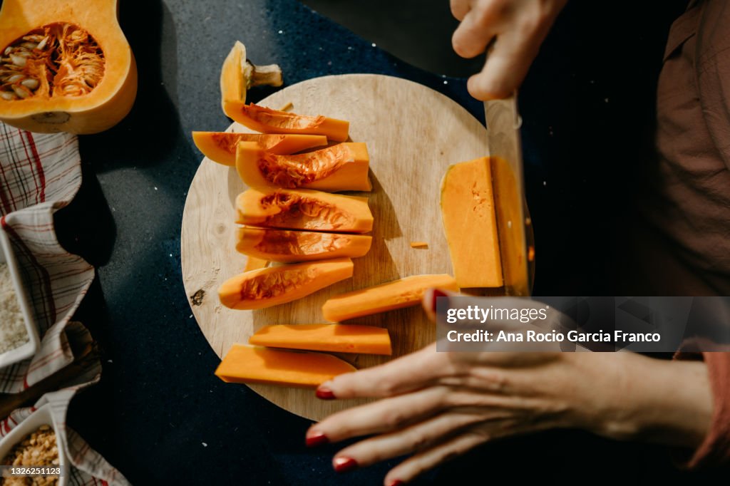 Caucasian woman slicing a Butternut Squash on a wooden cutting board.