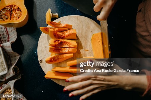 Caucasian woman slicing a Butternut Squash on a wooden cutting board. Caucasian woman slicing a Butternut Squash on a wooden cutting board.