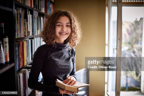 portrait of a smiling teenage girl holding book at home - 12 13 jahre mädchen stock-fotos und bilder