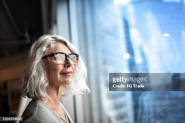 une femme d’affaires mature regarde par la fenêtre - monsieur et madame tout le monde photos et images de collection