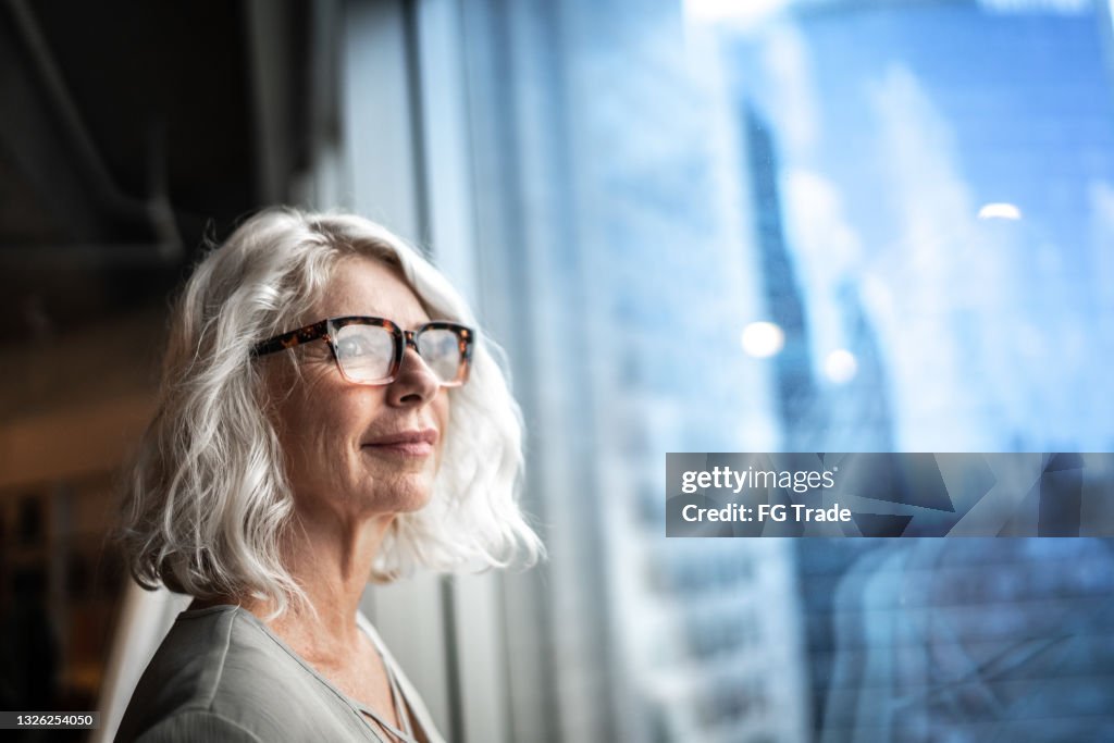 Donna d'affari matura che guarda fuori dalla finestra.