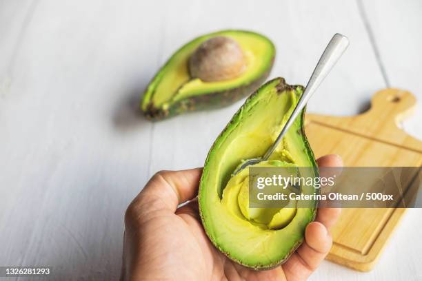 cropped hand of woman holding avocado on table - avocado stock-fotos und bilder