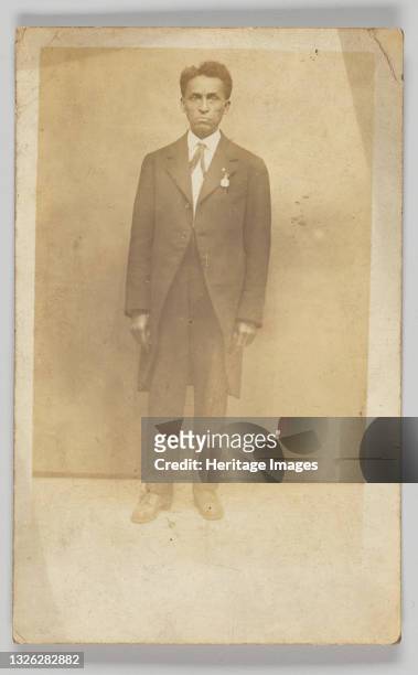 Photographic postcard of an unidentified man in a suit. The full-length photograph shows the man facing the camera with his hands at his side. Near...