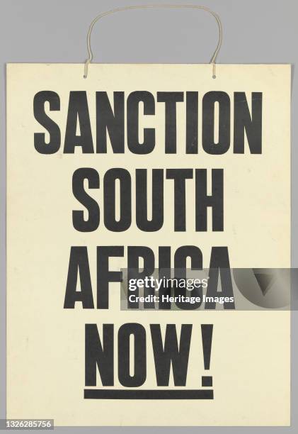 Protest sign calling for economic sanctions agains the apartheid regime of South Africa. The placard is somewhat larger than an average human torso,...