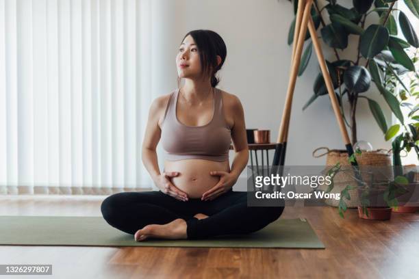 young asian pregnant woman practising yoga at home - prenatal yoga stock pictures, royalty-free photos & images