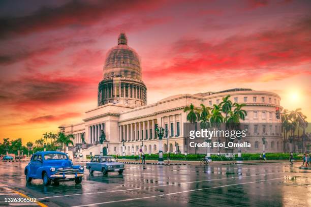 blue vintage car moving in front of el capitolio at sunset - capitolio stockfoto's en -beelden