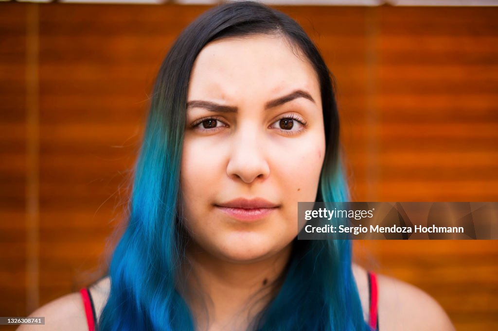 Young Latino woman with blue hair raising an eyebrow and looking at the camera