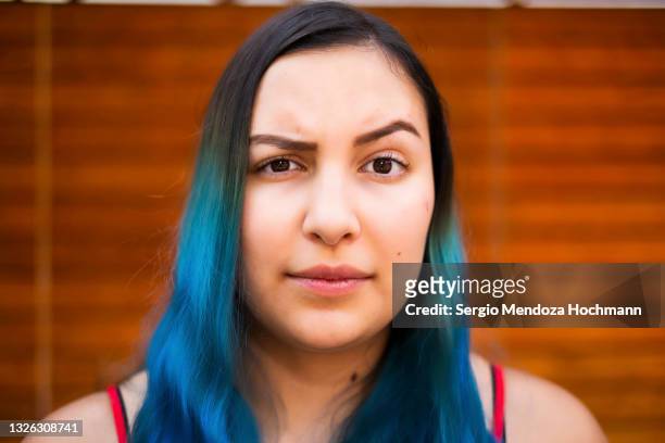 young latino woman with blue hair raising an eyebrow and looking at the camera - suspicion stock pictures, royalty-free photos & images