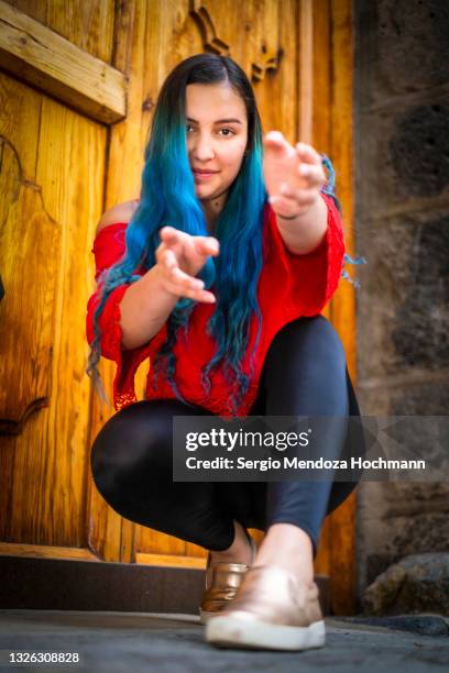 young latino woman with blue hair looking at the camera and squatting, crouching down and reaching with her hands towards the camera - woman reaching hands towards camera stock pictures, royalty-free photos & images