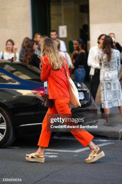 Guest wears a neon redshirt with flowers cut-out details, neon orange flared pants, beige large cotton shoulder bag, beige wicker strappy platform...