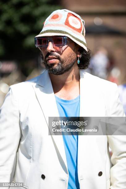 Guest with Nike blue shirt, white blazer. Knitted hat, and blue sunglasses seen at Fortezza Da Basso on June 30, 2021 in Florence, Italy.