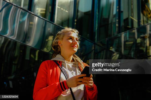 young woman with dreadlocks in red jacket taking photo with her cell phone.. - red jacket stock pictures, royalty-free photos & images