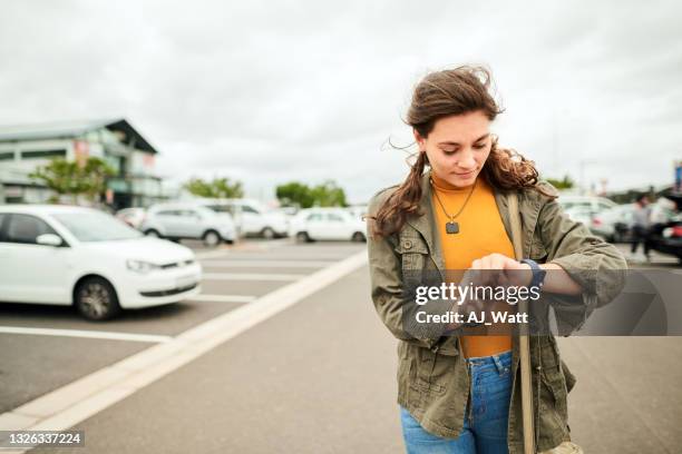 young woman checking the time on her watch in a parking lot - impatient stock pictures, royalty-free photos & images