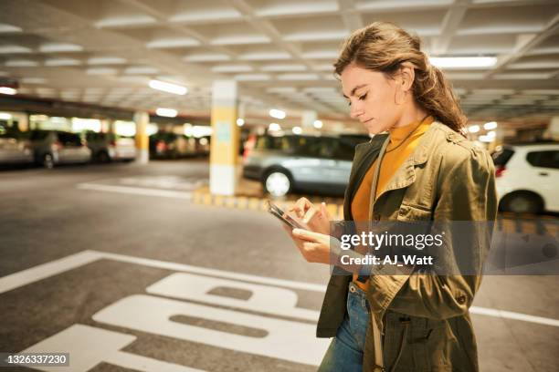 mujer revisando una aplicación de teléfono mientras camina en un garaje de estacionamiento - car park fotografías e imágenes de stock