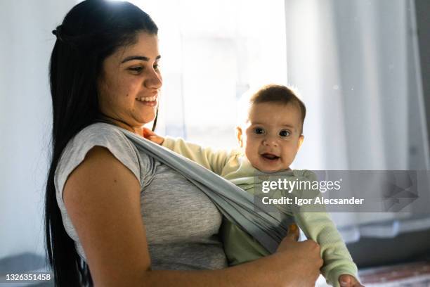 mother carrying baby in sling at home - baby carrier stock pictures, royalty-free photos & images