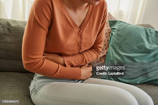 foto de una mujer que experimenta dolor de estómago mientras está acostada en el sofá de casa - indigestión fotografías e imágenes de stock