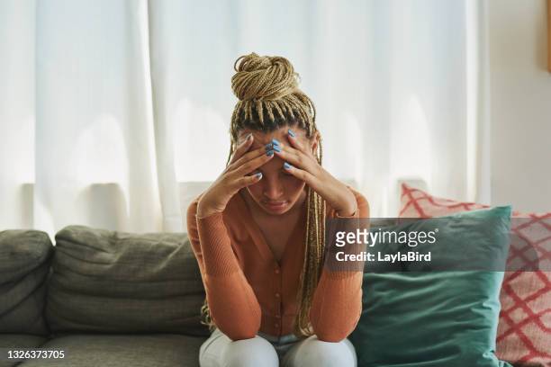 schuss einer jungen frau, die traurig auf dem sofa zu hause aussieht - stressed young woman sitting on couch stock-fotos und bilder