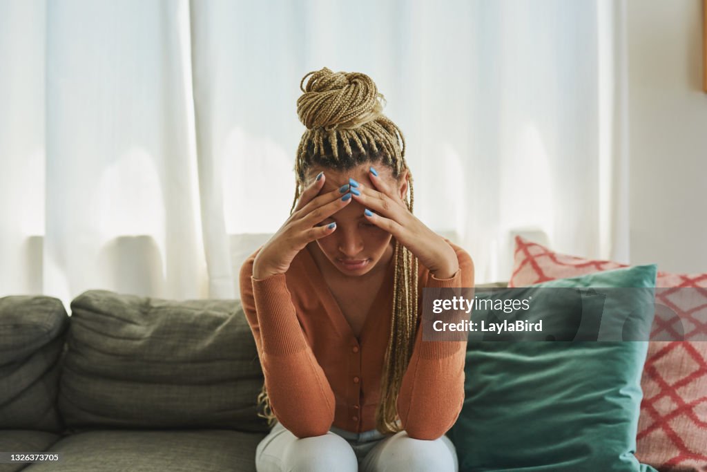Shot of a young woman looking sad on the sofa at home